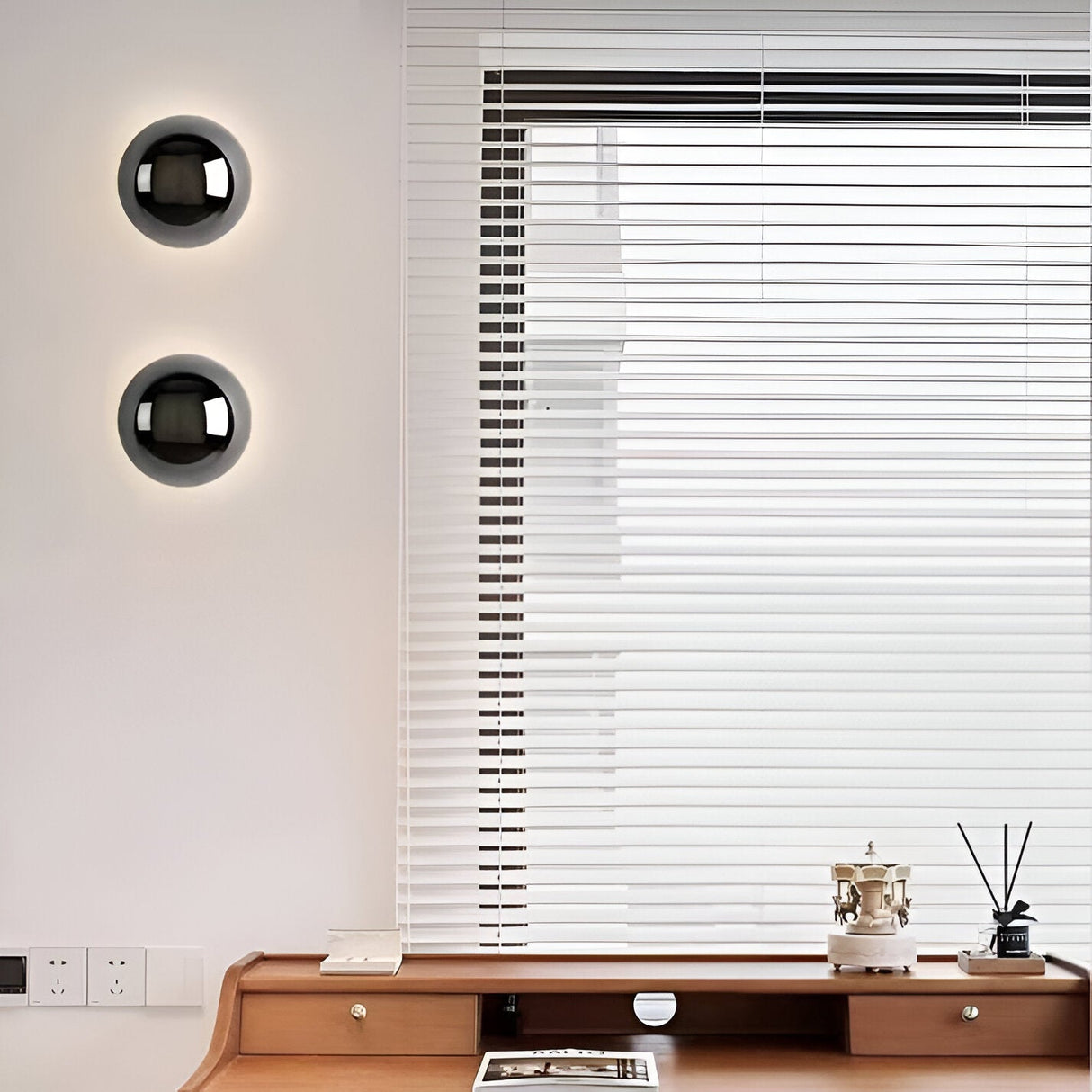 Two small silver dome sconces on a wall beside a window blind