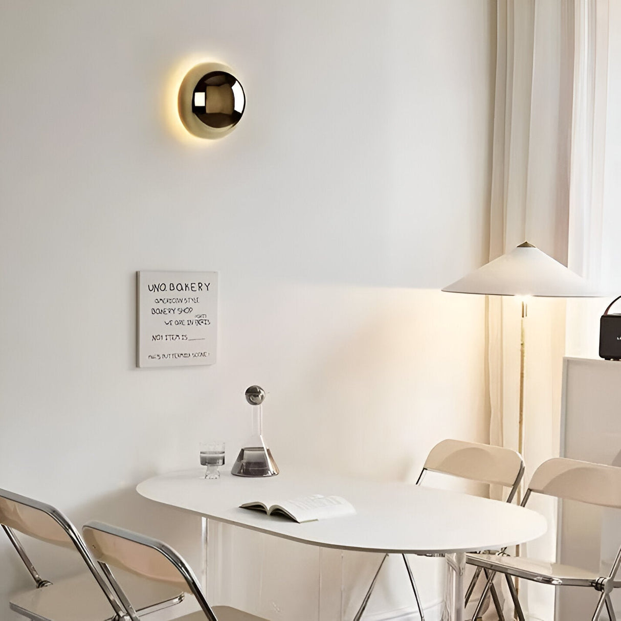 Mirrored dome sconce lit on a white wall above a dining table