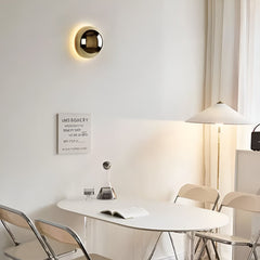 Mirrored dome sconce lit on a white wall above a dining table