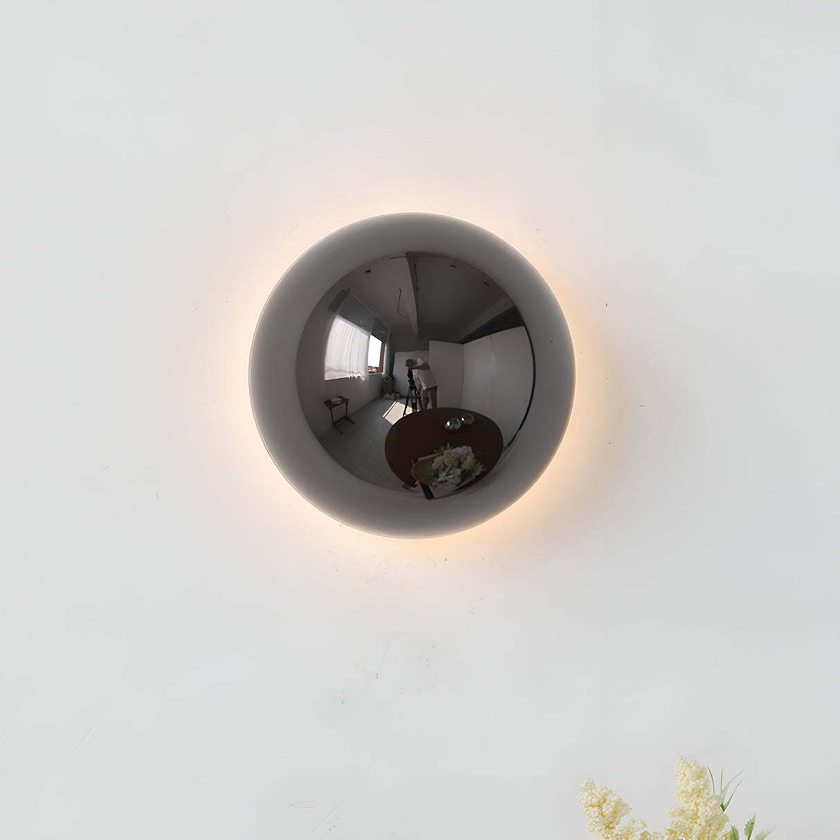 Silver dome sconce lit on a white wall with a soft ring of light