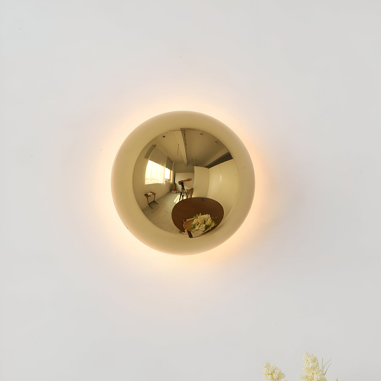 Gold mirrored dome sconce lit on a white wall with a warm halo