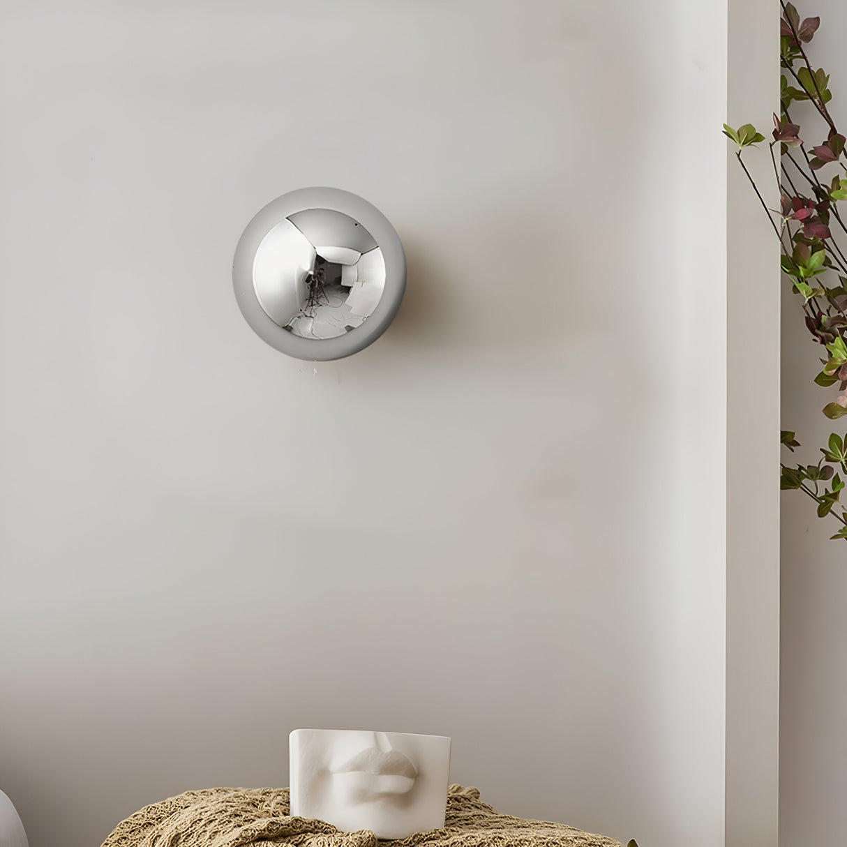Silver dome sconce lit beside a hanging plant on a white wall