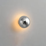 Gold dome sconce lit on a white wall beside dried grasses
