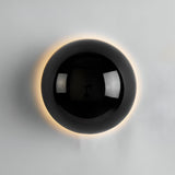 Silver dome sconce lit on a white wall beside a potted palm