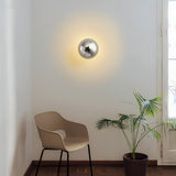 Two gold dome sconces lit above a dining table with green chairs
