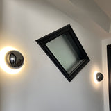 Silver dome sconce lit beside a black framed skylight window