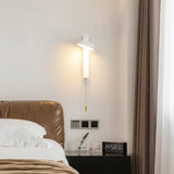 White rotating sconce lit beside a bed and a bedside clock