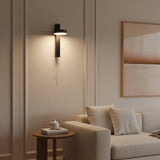 Black bar sconce with a silver pull chain and a lit disc head