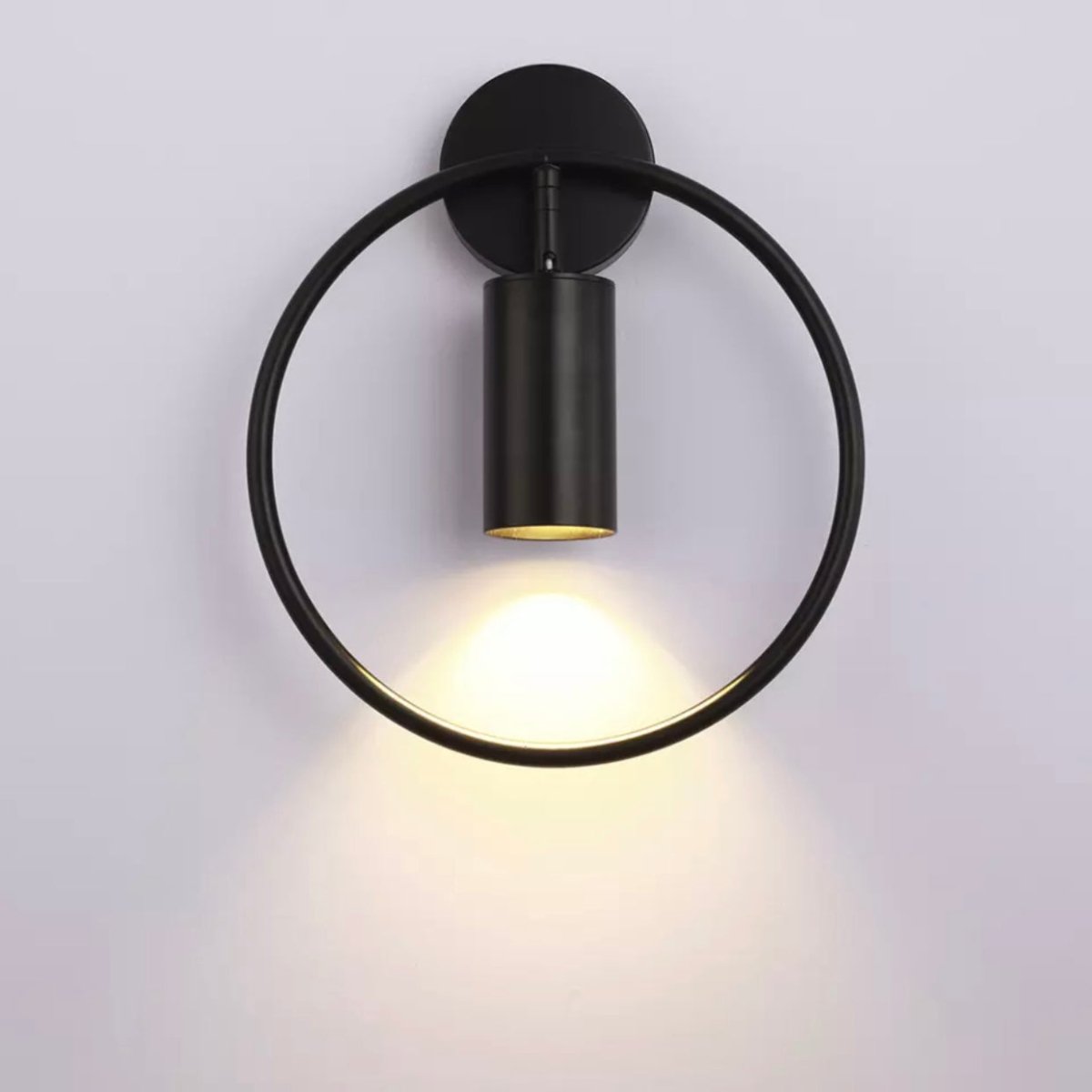 Black ring wall sconce with a black spot lit on a pale wall