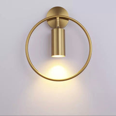 Brass ring wall sconce with a brass spot lit on a pale wall