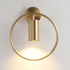 Brass ring wall sconce lit against a plain pale wall