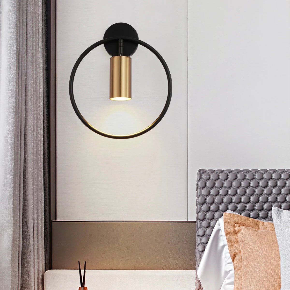 Brass ring wall sconce lit beside a tall mirror and a grey headboard