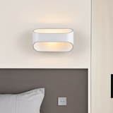 White oval sconce lit on a pale wall beside a bed