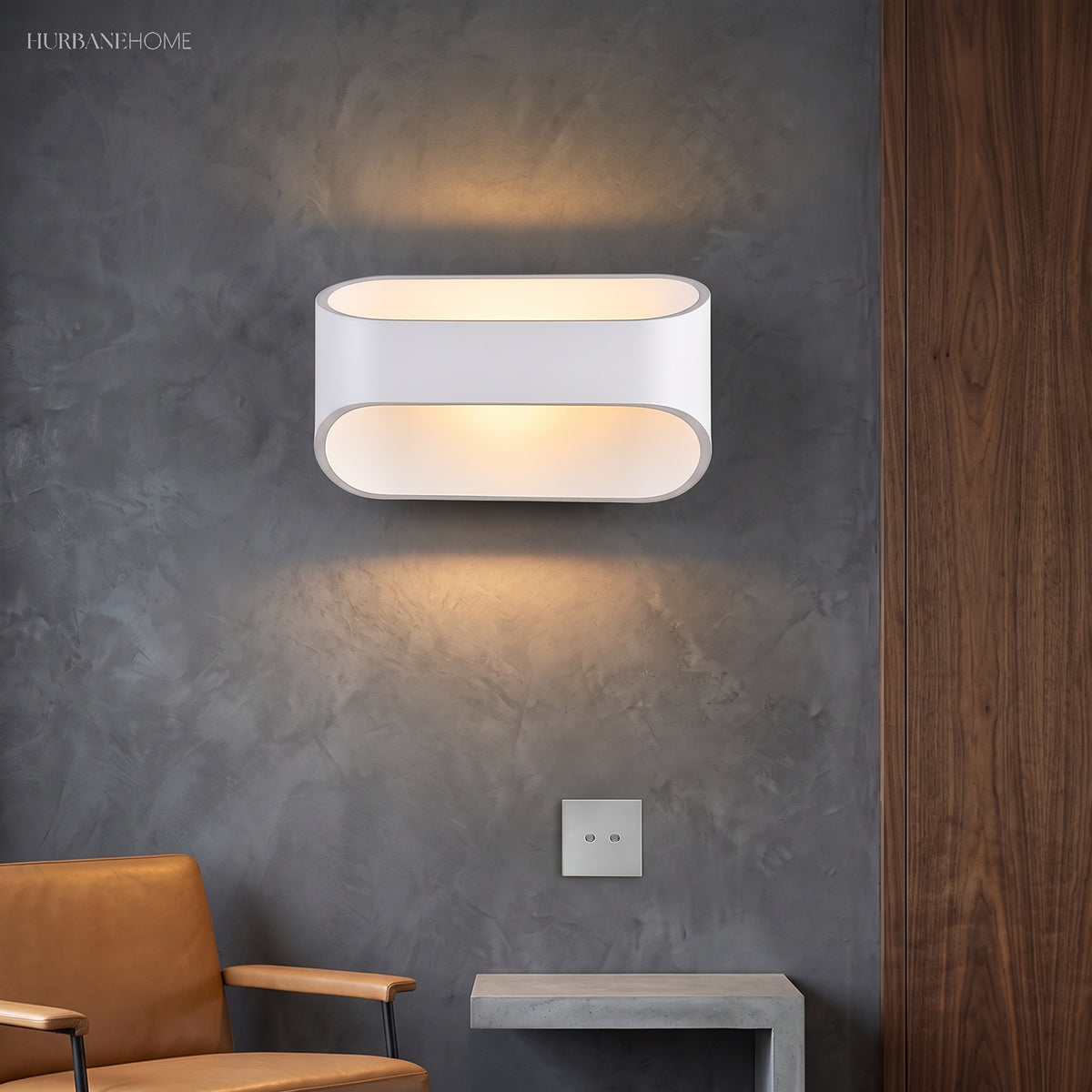 White oval sconce lit on a dark plaster wall above a chair