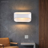 White oval sconce lit on a dark plaster wall above a chair