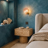 Amber shell wall sconce glowing on a deep blue bedroom wall above a wooden nightstand