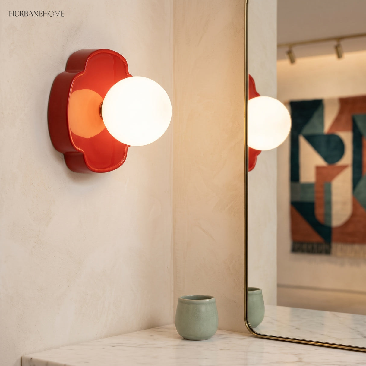 Red orb wall sconce lit beside a gold-framed mirror on cream plaster