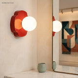 Red orb wall sconce lit beside a gold-framed mirror on cream plaster