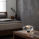 Glowing oval glass lamp on a bedroom nightstand near a bed