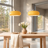 Two yellow oval glass pendant lights over a wood dining table by windows