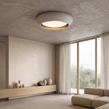 Light grey cement flush mount ceiling light glowing warmly in a minimalist living room
