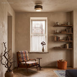 Travertine flush mount ceiling light glowing above a plaster room with a mid-century chair