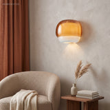 Orange glass sconce casting warm light above a boucle armchair and side table