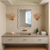 Two amber shell sconces beside a wavy mirror over a neutral bathroom vanity