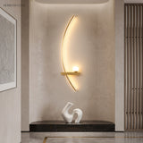 Gold curved linear wall sconce glowing warm above a hallway console table