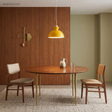 Yellow bell pendant light over a walnut dining table against a wood panel wall