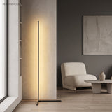 Black minimalist LED floor lamp lighting a corner near a boucle chair and framed art