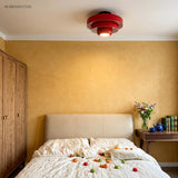 Red tiered ceiling light in a warm yellow bedroom above a bed