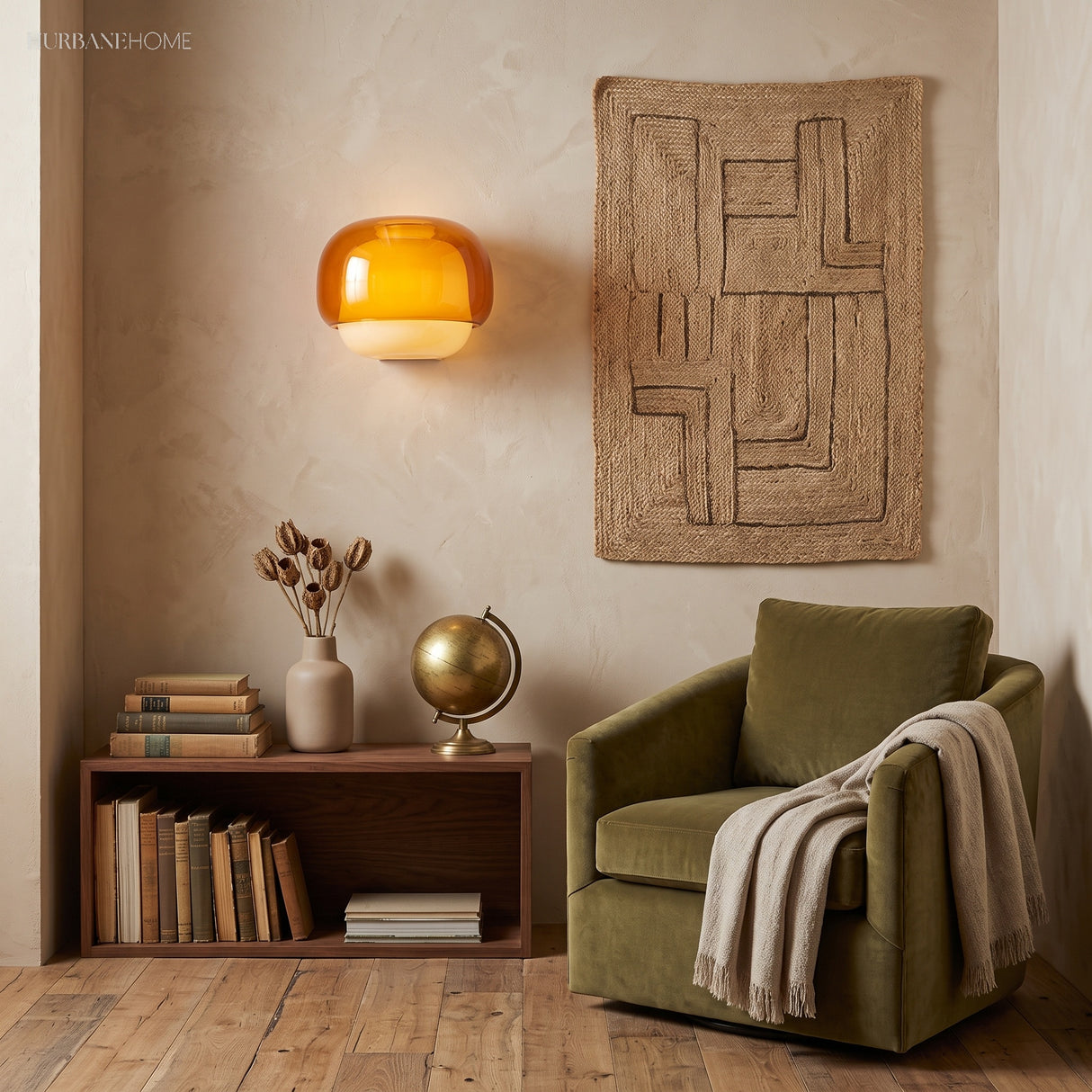 Amber wall sconce beside a woven jute hanging and green velvet armchair