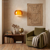 Amber wall sconce beside a woven jute hanging and green velvet armchair