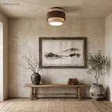Stone and walnut ceiling light lighting a rustic entryway with a wooden bench and ink art