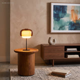 Warm-lit glass table lamp on a round walnut side table in a living room