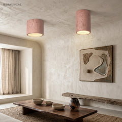 Two soft pink cylindrical ceiling lights above a rustic wooden bench and artwork
