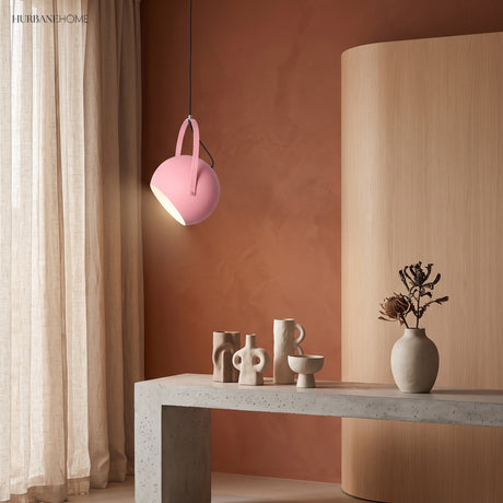 Rose pink ball pendant light tilted against a warm terracotta plaster wall