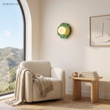 Green glass globe wall sconce in a sunny reading nook with boucle chair