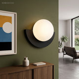 Black glass globe wall sconce lit on a green wall beside framed art