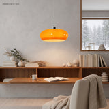 Orange glass pendant light glowing above a wooden reading shelf in a study