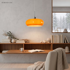 Orange glass pendant light glowing above a wooden reading shelf in a study