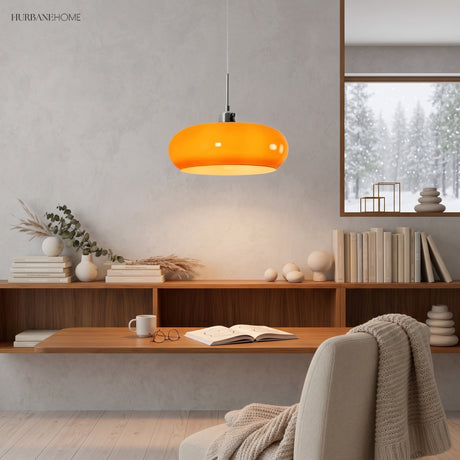 Orange glass pendant light glowing above a wooden reading shelf in a study