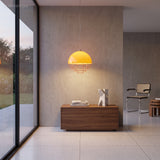 Lit orange pendant with layered discs hanging over a walnut sideboard against a concrete wall