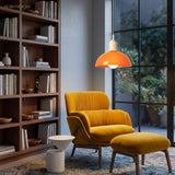 Orange bowl pendant light glowing above a mustard reading chair and shelves