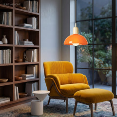 Orange bowl pendant light glowing above a mustard reading chair and shelves