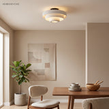 White tiered ceiling light above a walnut dining table and boucle chair