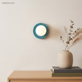 Blue round wall sconce lit beside dried eucalyptus stems on an oak sideboard