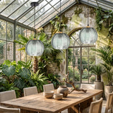 Three green glass globe pendants hanging in a plant filled glasshouse dining room