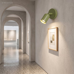 Green rotatable spotlight sconce lighting a framed print in a plaster hallway